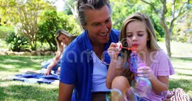 爸爸和女儿在<strong>公园</strong>野餐时用<strong>泡泡</strong>棒吹<strong>泡泡</strong>